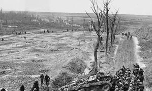 Troops passing shattered trees and ruins on the Western Front.